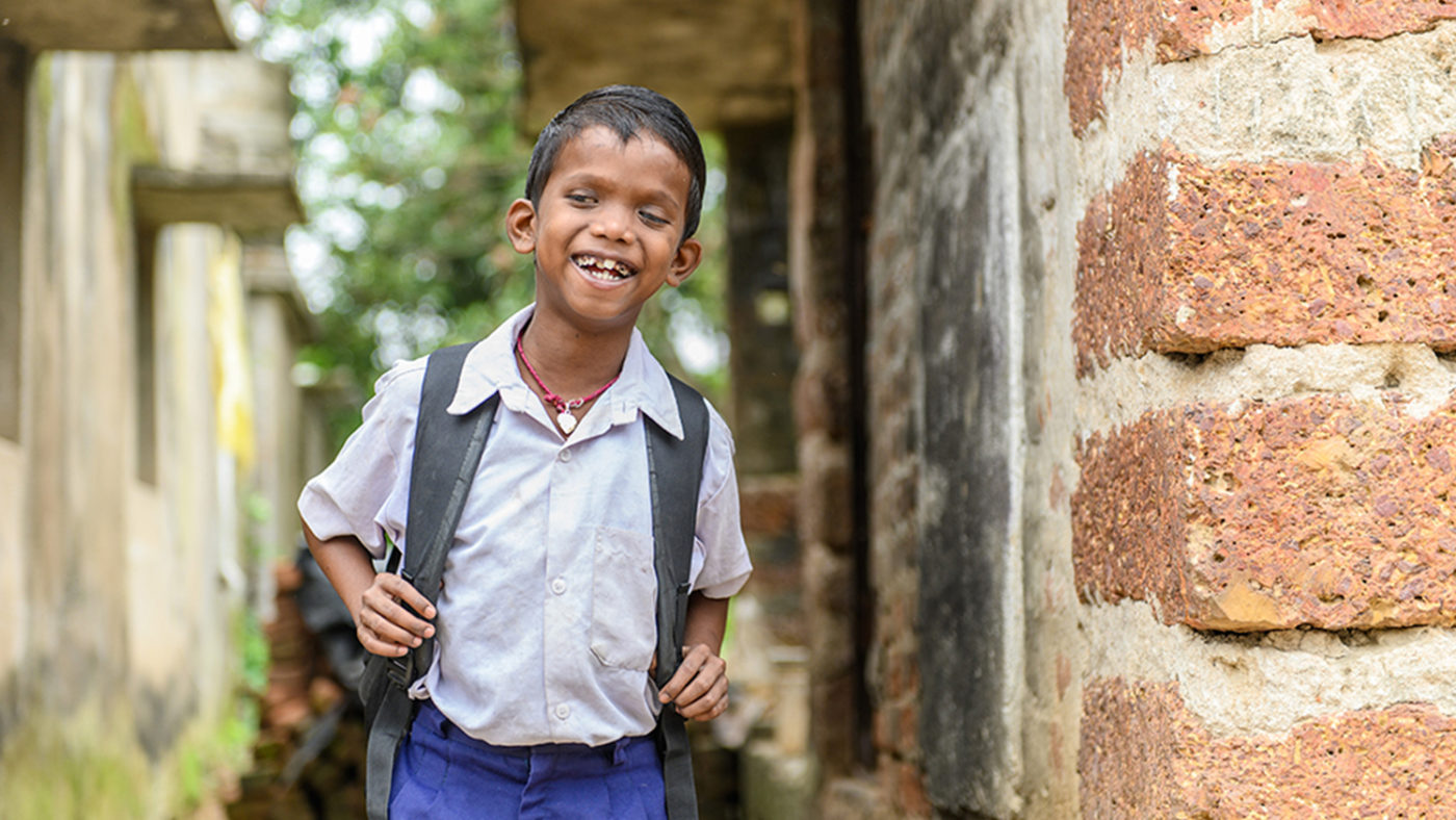 Sanjit happily looks towards the camera as he independently walks towards school.