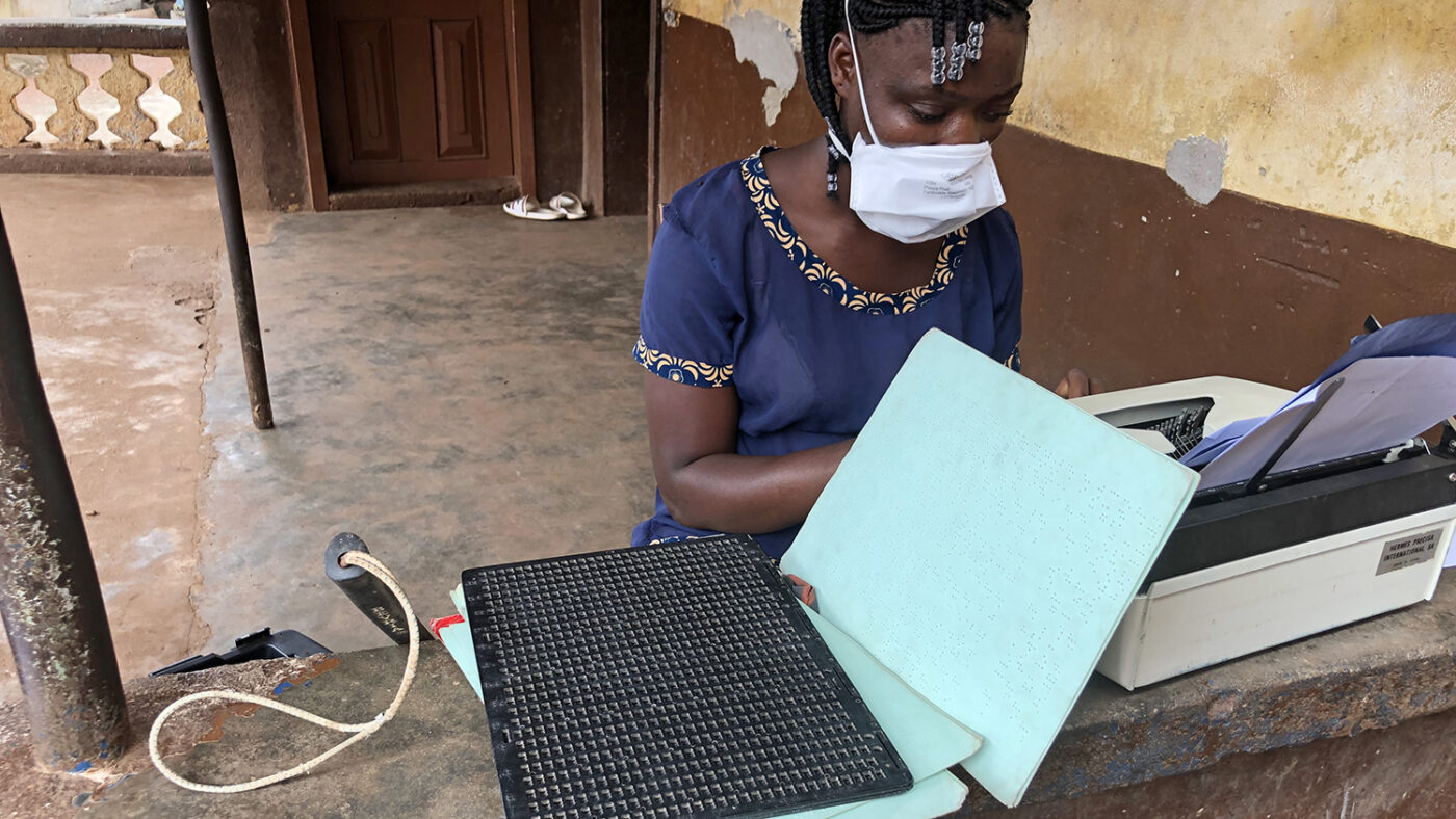 A girl with a face mask on, next to braille writing material.
