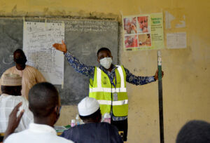 A man wearing a mask gives a demonstration to distributors in a school classroom.