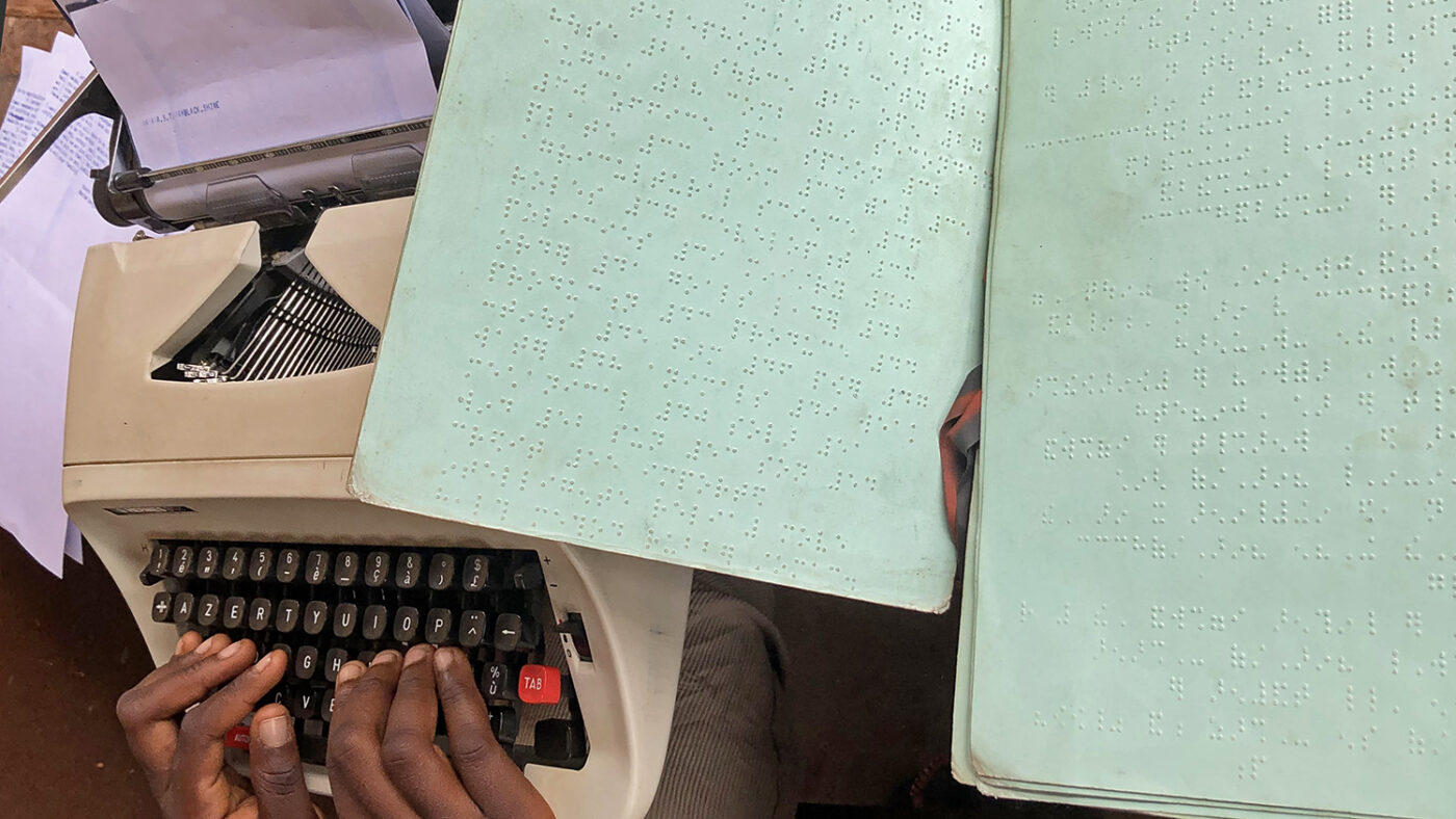 Hands on a braille typewriter and sheets of braille notes.