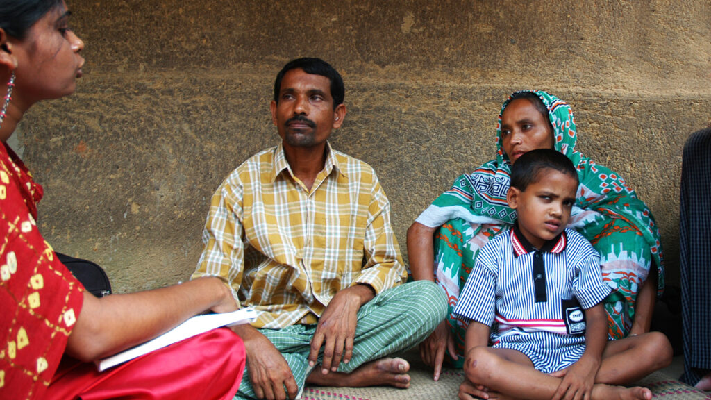 A young boy squinting, sitting on the floor next to three adults.