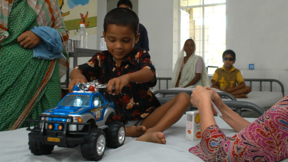 A boy sitting on a hospital bed, playing with a toy truck.