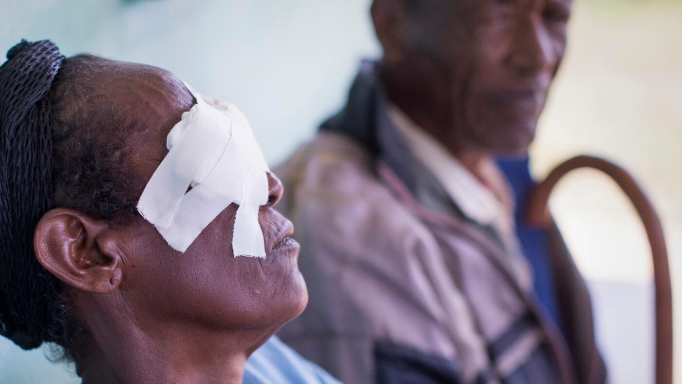 Side profile of a lady with bandages over her eyes, holding a walking stick.