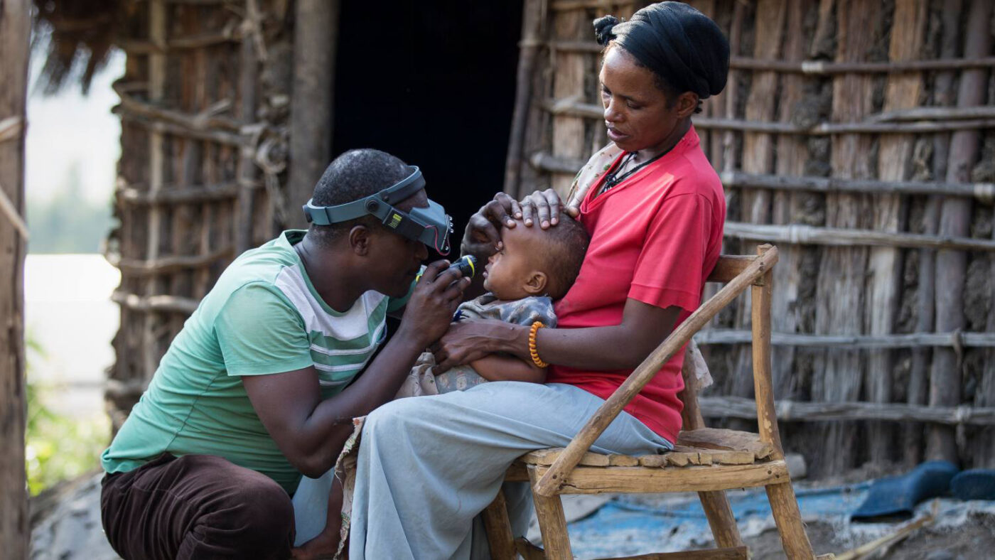 A young child sits on his mother's knee while getting his eyes tested.