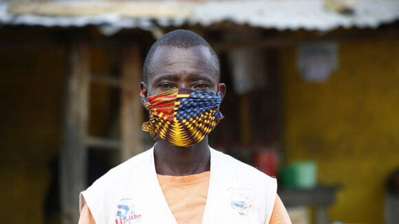 A male healthcare worker stands outside wearing a colourful face mask and a white coat.