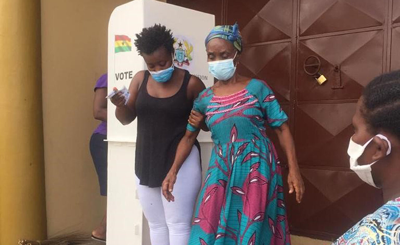 A woman assists another woman to walk down some steps. Both women are wearing face masks.