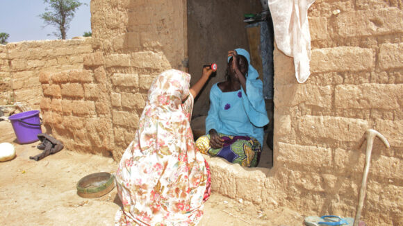 Case finder Surayya holds a torch while examining a woman's eyes (Zuraira's) who is holding up her eyelid.