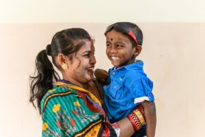 A young boy, Omm, smiles being held by his mother.