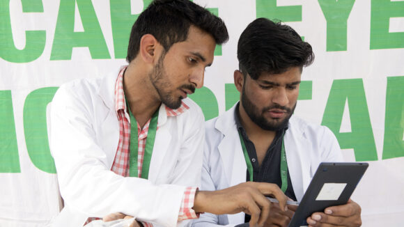 Two vision technicians from the India Truckers Eye Health Programme look at a handheld tablet.