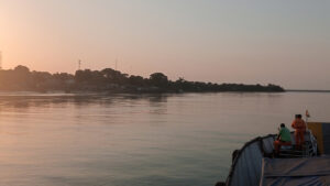 The view from the deck of a boat, with a sunset and land in the distance.