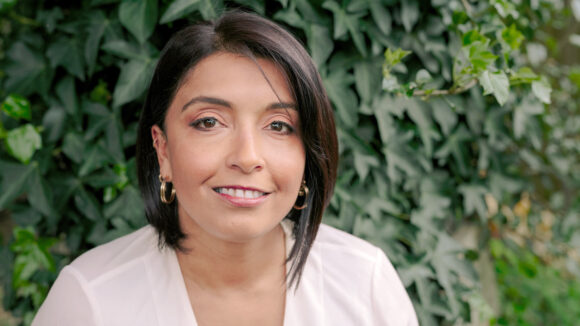 Actress Sunetra Sarker smiling in front of a leafy green wall.