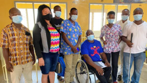 A group of eight people together, all wearing masks. One person is holding a white cane and one person is a wheelchair user.