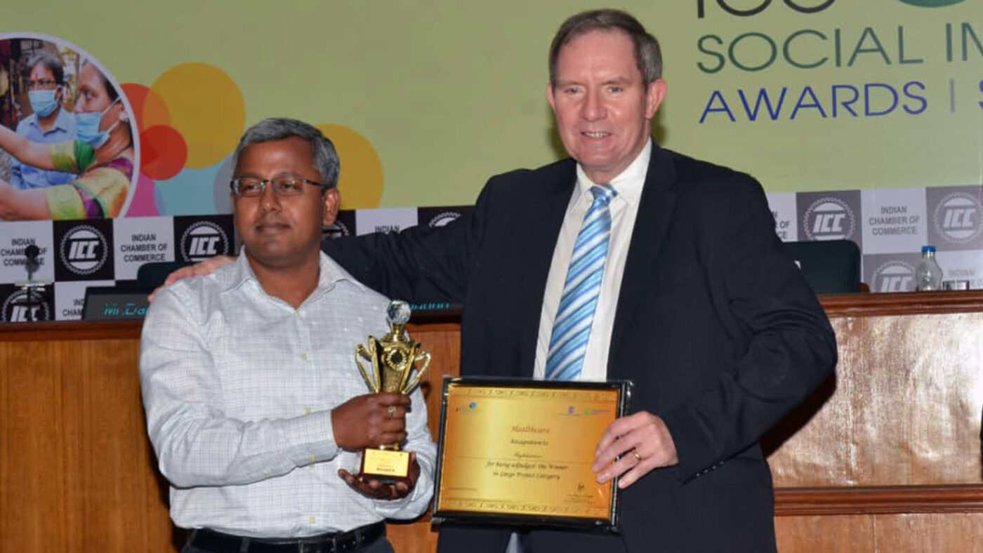 A man wearing a suit presents a plaque and trophy to another man.