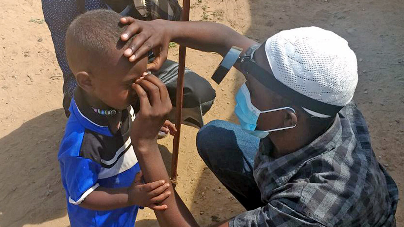 An eye health worker wearing a mask checks a boy's eyes.