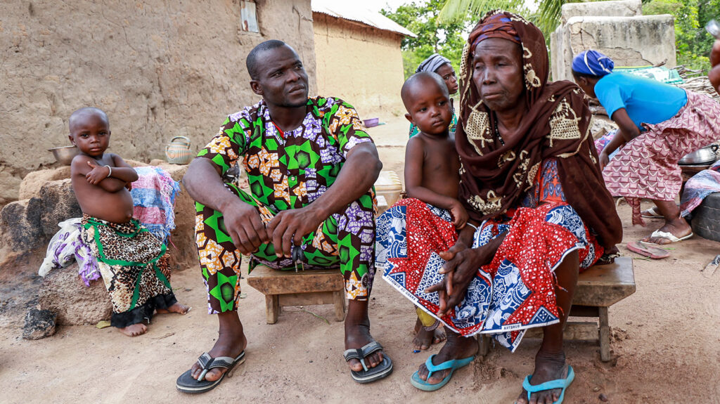 An older woman sits outside surrounded by her family.