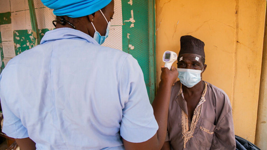 A man wearing a face mask has his temperature taken by a health worker.