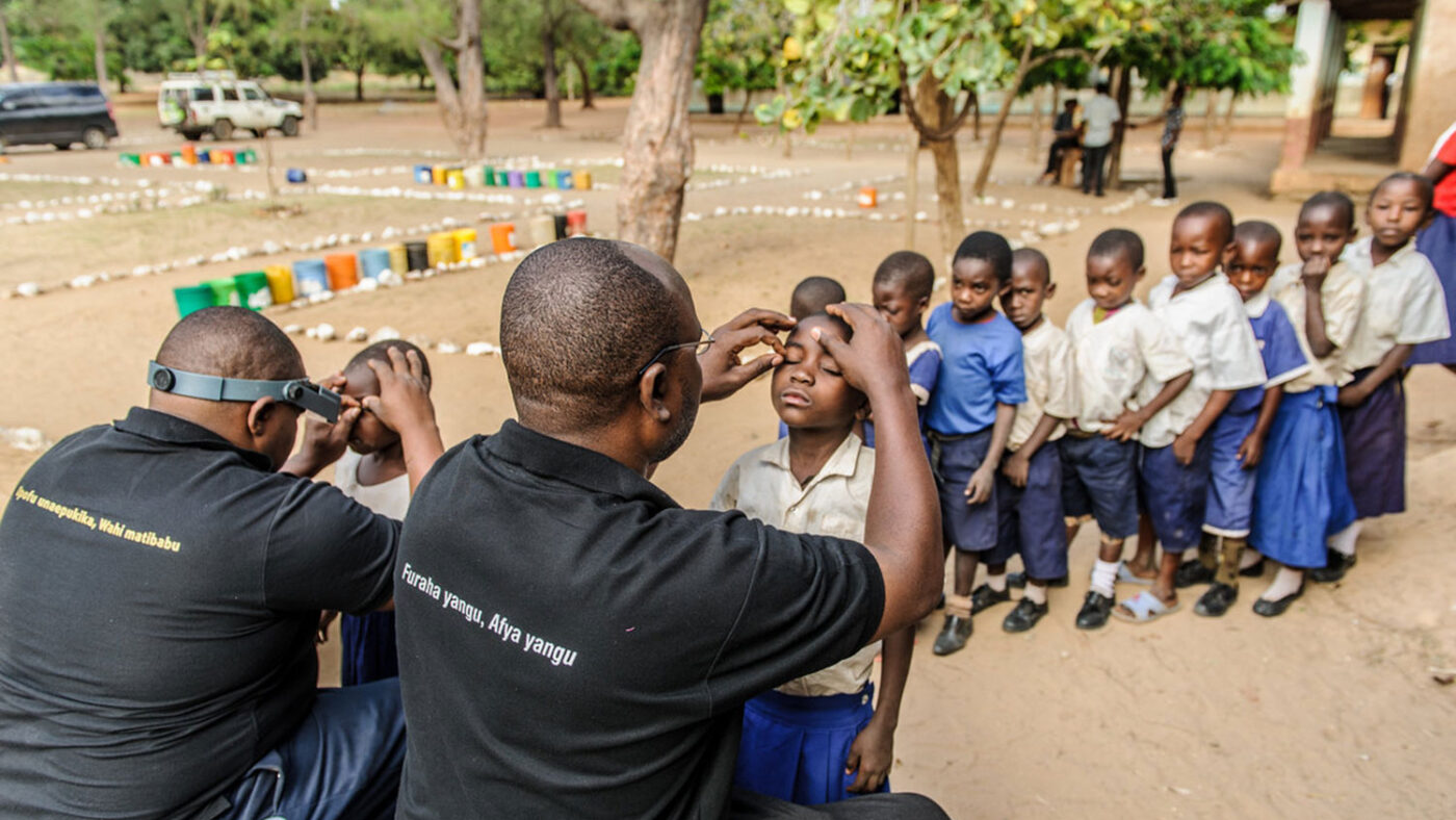 A queue of school children in uniform line up to receive an eye examination.