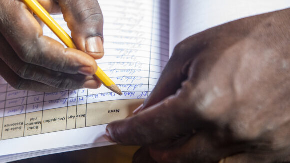 A close-up of a researcher's hands writing notes into a form in French.