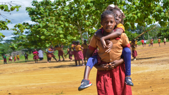 A school student in Cameroon gives her classmate a lift on her back in the playground.