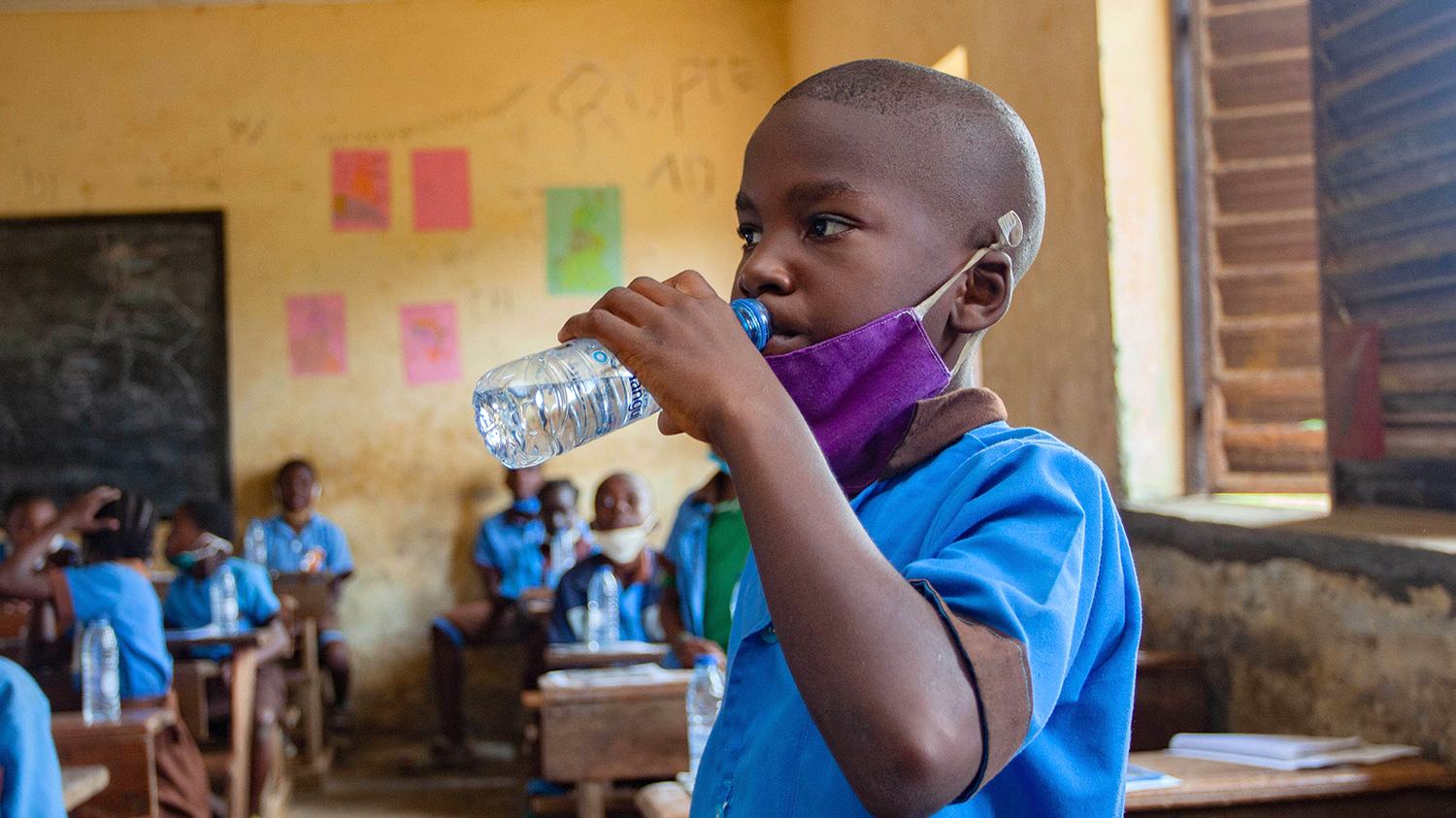 In Cameroon, a schoolboy in a classroom has a drink of water after taking deworming medication.
