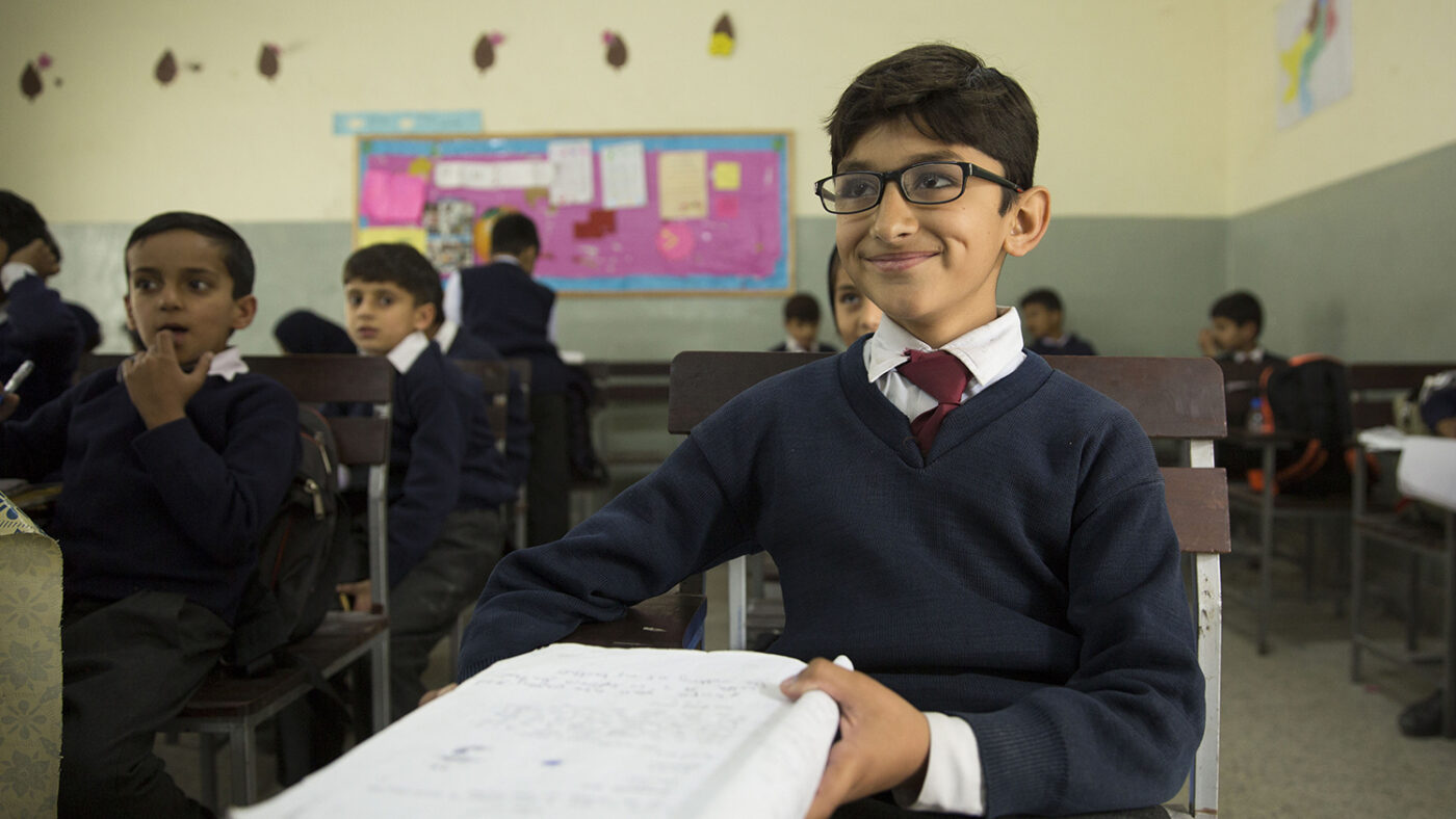 A school student in the classroom smiles while wearing his new glasses.