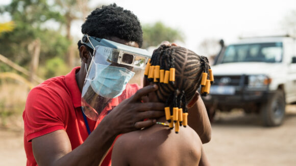 An eye health worker wearing a mask and visor checks a child's eyes for signs of trachoma.