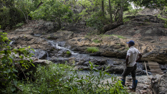 A man stands on a river bank looking at the flowing water.