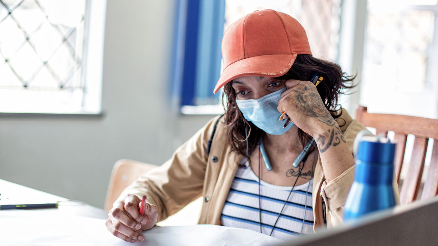 Divinah sits at a desk in a classroom, with a pen in her hand.