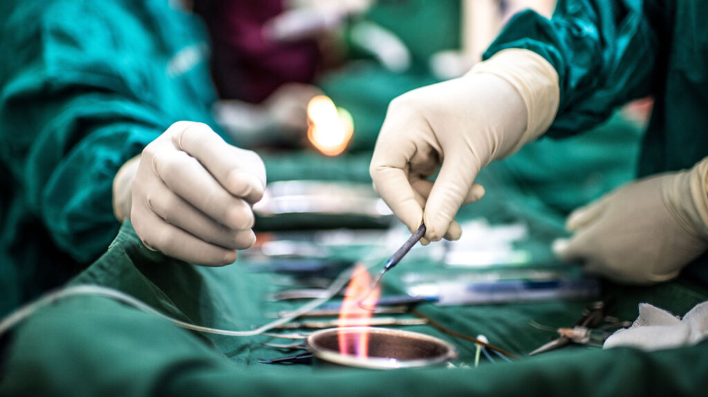 A close-up of two surgeons' hands during an operation as they handle surgical equipment, They're wearing green scrubs.