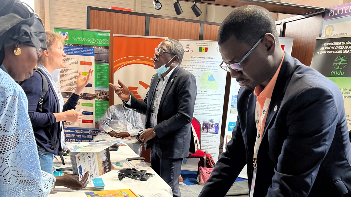 Two men behind a conference table talk to attendees.