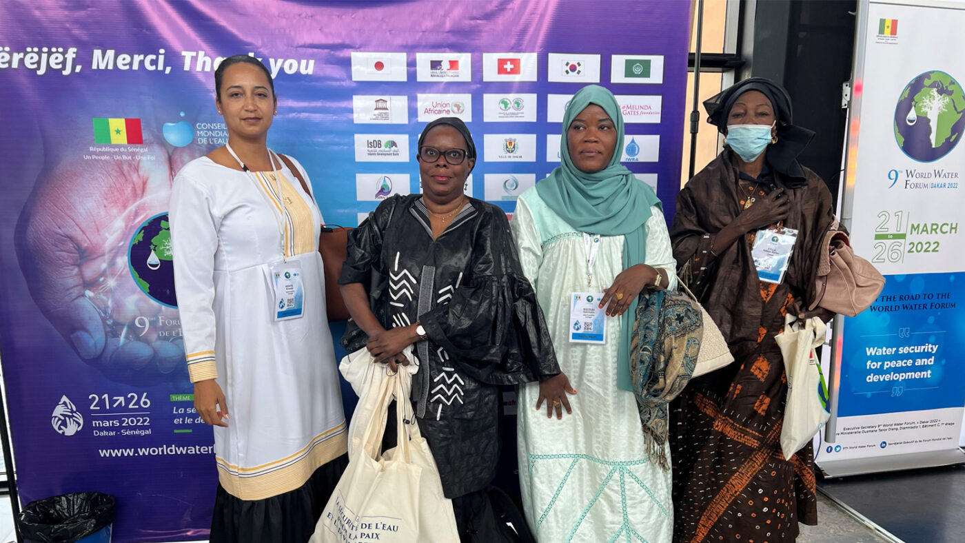 Four women look to the camera in front of a World War Forum board.