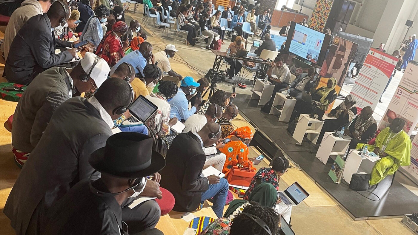 A crowd of people on raked seating look towards a stage of presenters.