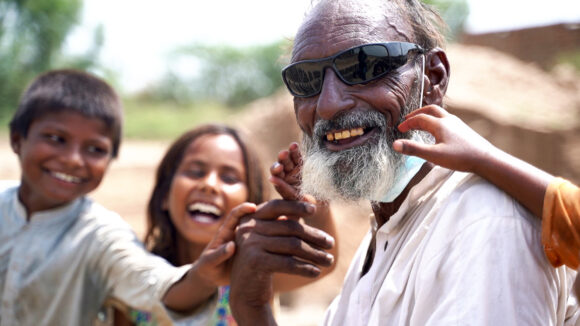 A man wearing sunglasses smiles with his two happy grandchildren.