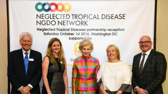 Princess Alexandra stands with Dr Caroline Harper and other staff members in front of a banner for the Neglected Tropical Disease Network.