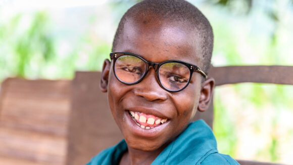 A young boy smiles broadly. He's wearing glasses.