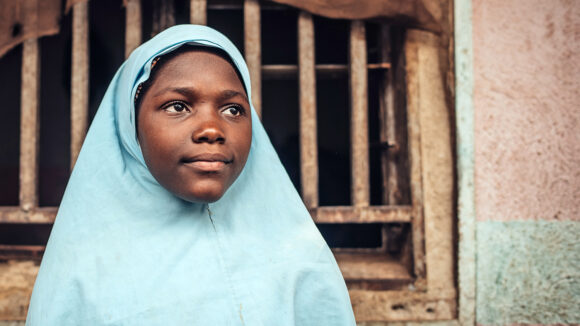 Asmau at home. She wears a bright blue headscarf.