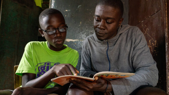 Arthur reads a book that is being held by his father.
