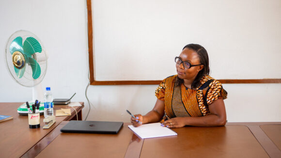 Gladys sits at a large desk writing a letter.