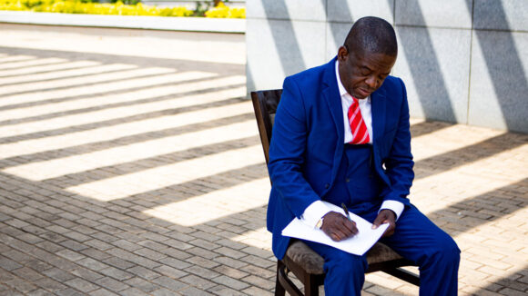 Michael sits on a chair outside writing a letter.