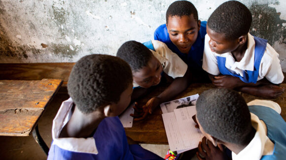 Schoolchildren huddle together around a desk to write a letter.