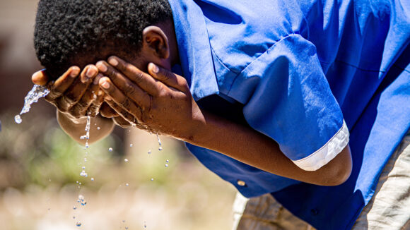 A school student wearing bright blue uniform washes their face.