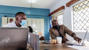 Nicodemus and a classmate sit at a desk discussing something on a laptop screen.