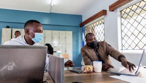 Nicodemus and a classmate sit at a desk discussing something on a laptop screen.