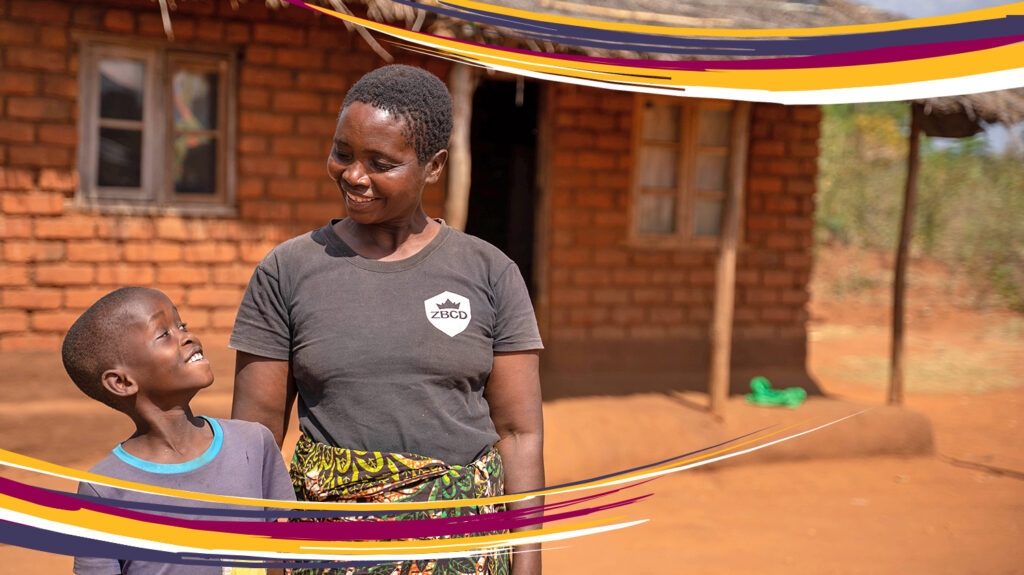 Rose and her grandson Jonathan outside their home in Malawi. They're looking at one another and smiling.