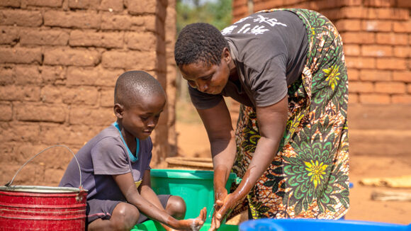 Rose and Jonathan wash their hands together in a bowl of water outside their home.