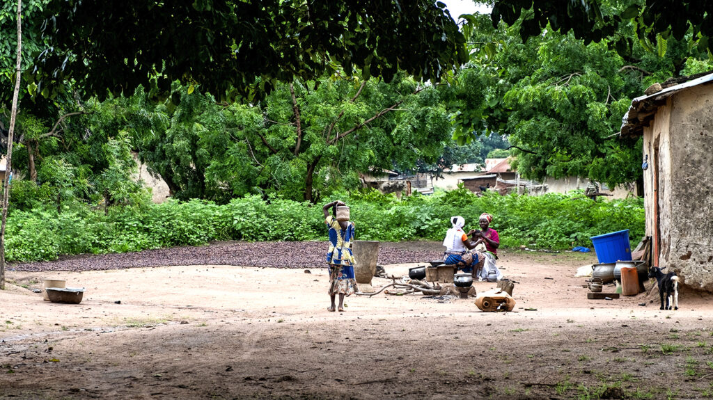 A rural village in Benin, with dusty roads and lush vegetation in the background.