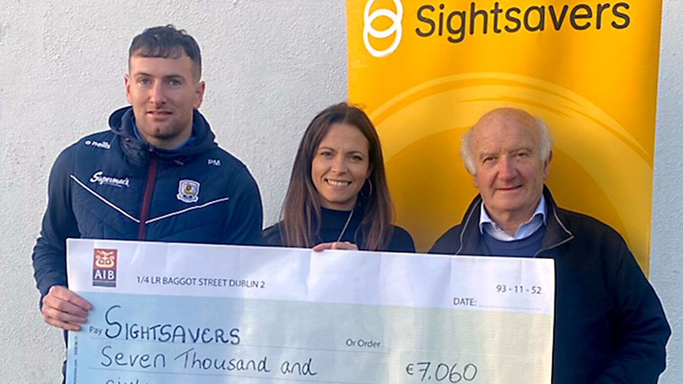 Two men and a woman stand smiling and holding a large cheque made out to Sightsavers for €7,060.