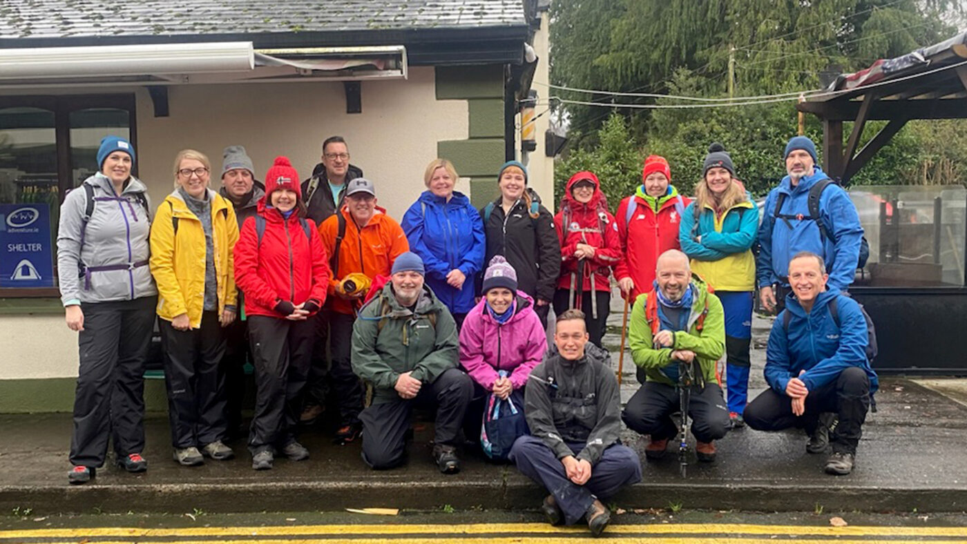 A large group of men and women wearing outdoor clothing gathers for a photo before hiking in the Wicklow mountains.