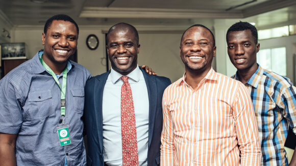 Four men smile broadly. They're all dressed in smart professional clothing.
