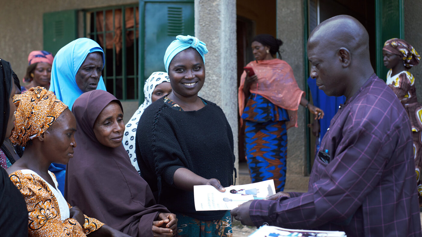 A group of mothers are handed a parent support guide by a teacher at an inclusive school in Nigeria.